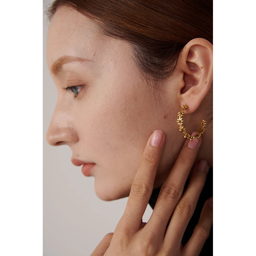 Close-up of a person wearing a gold hoop earring with a neutral background