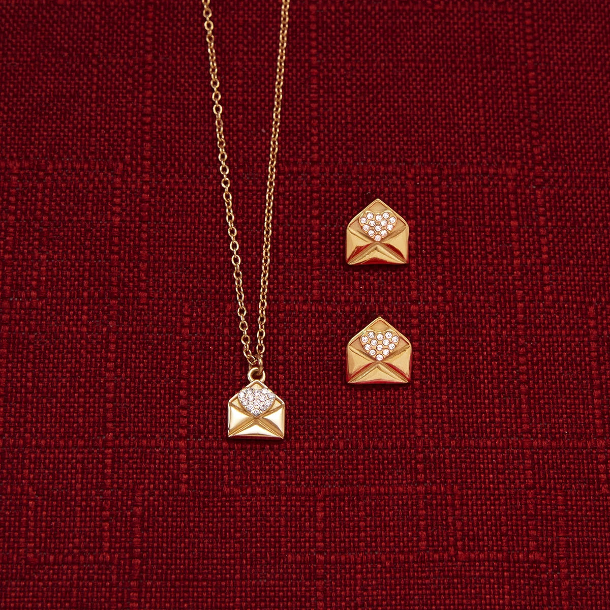 Gold heart envelope necklace and earrings on a red textured background