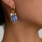 Gold earring with a blue and white floral design on a person's ear against a neutral background