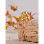 Gold ring with gemstones on a textured surface with blurred autumn leaves in the background