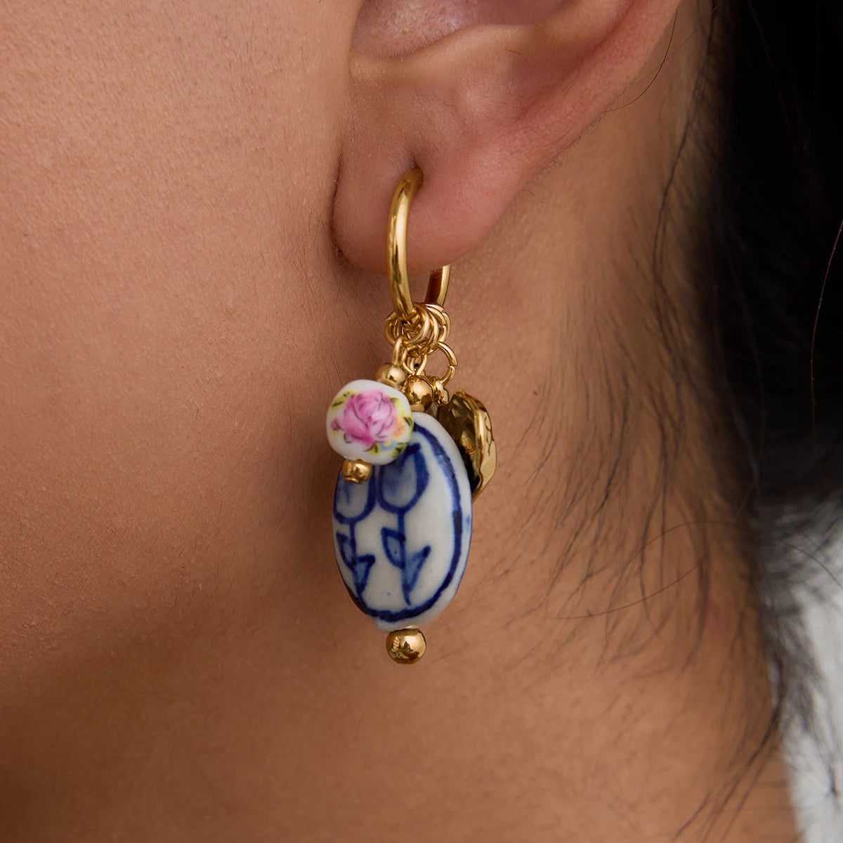 Close-up of an ear wearing a gold hoop earring with a decorative charm.