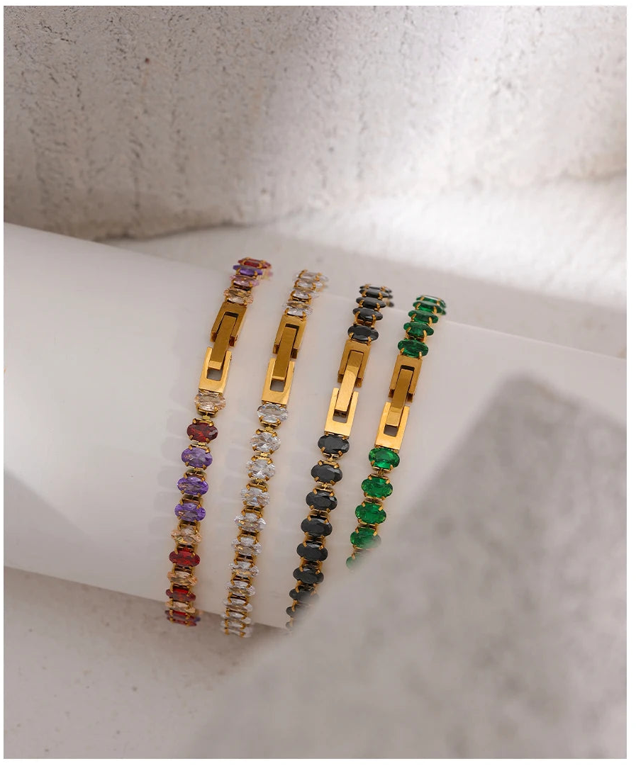 Three gold bracelets with colorful stones on a white surface
