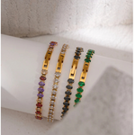 Three gold bracelets with colorful stones on a white surface