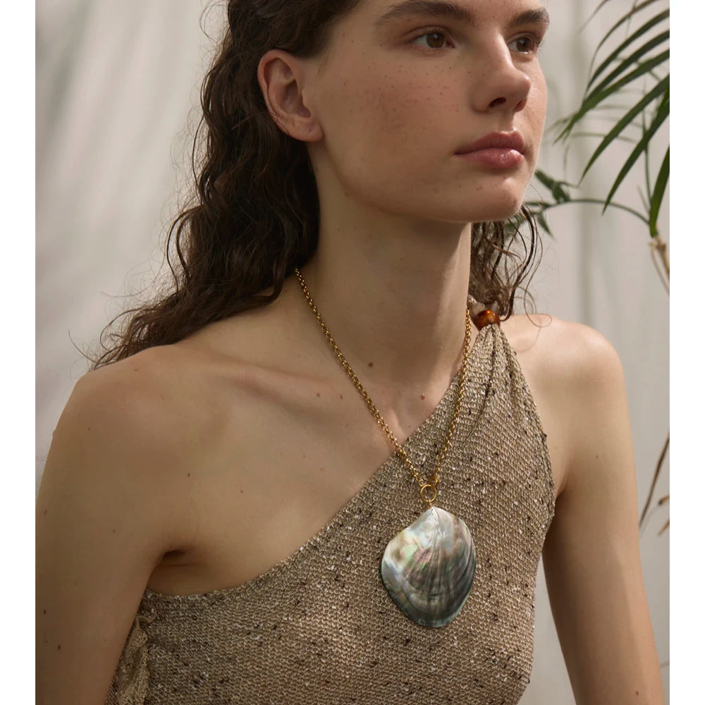Woman wearing a gold necklace with a large pendant against a neutral background