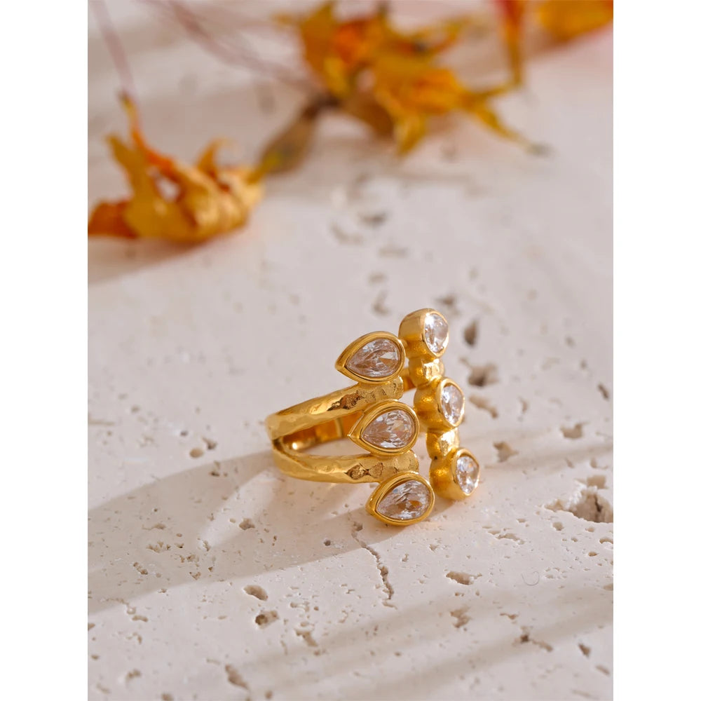 Gold ring with clear stones on a textured surface with dried flowers in the background