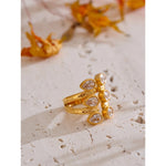 Gold ring with clear stones on a textured surface with dried flowers in the background