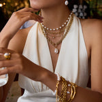 Woman wearing multiple gold and pearl necklaces and bracelets against a blurred background