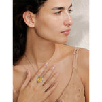 Woman wearing a gold necklace with a pendant, touching her chest.