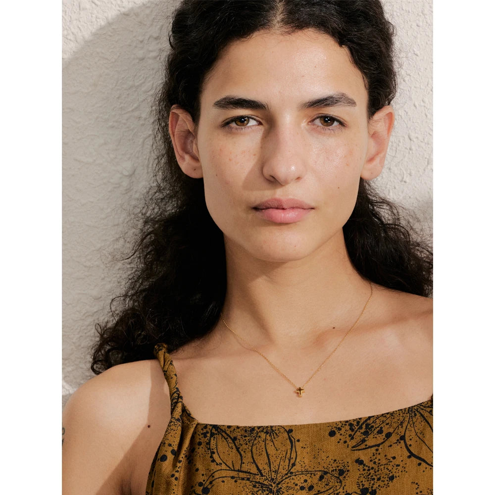 Woman wearing a gold necklace against a neutral background