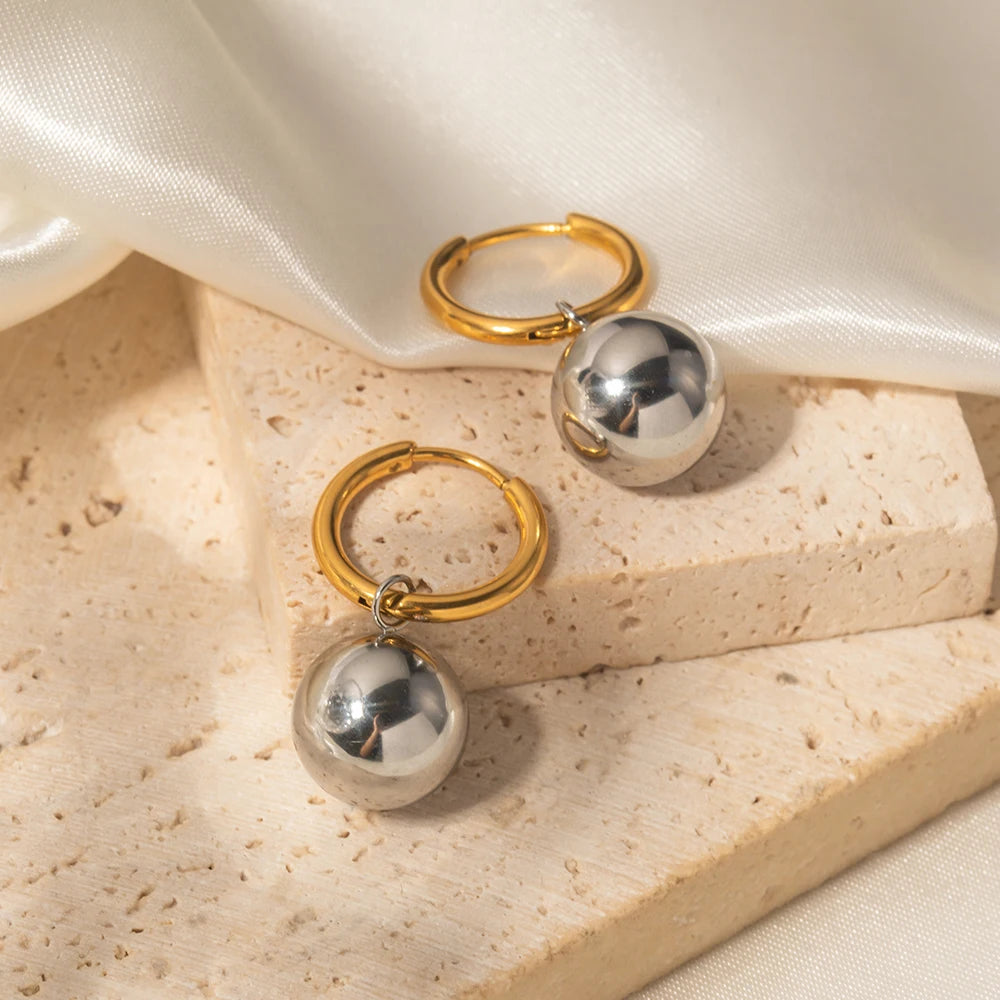 Gold hoop earrings with silver spherical charms on a beige surface.