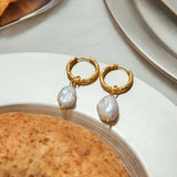Gold hoop earrings with pearl drops on a white plate.