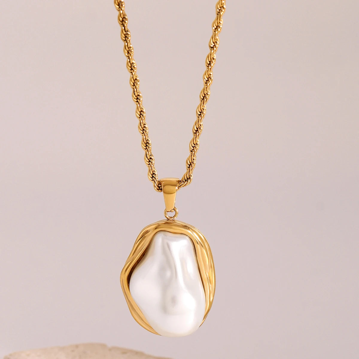 Gold necklace with a large pearl pendant on a beige background