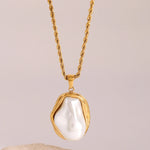 Gold necklace with a large pearl pendant on a beige background
