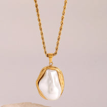 Gold necklace with a large pearl pendant on a beige background