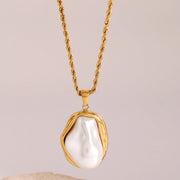 Gold necklace with a large pearl pendant on a beige background
