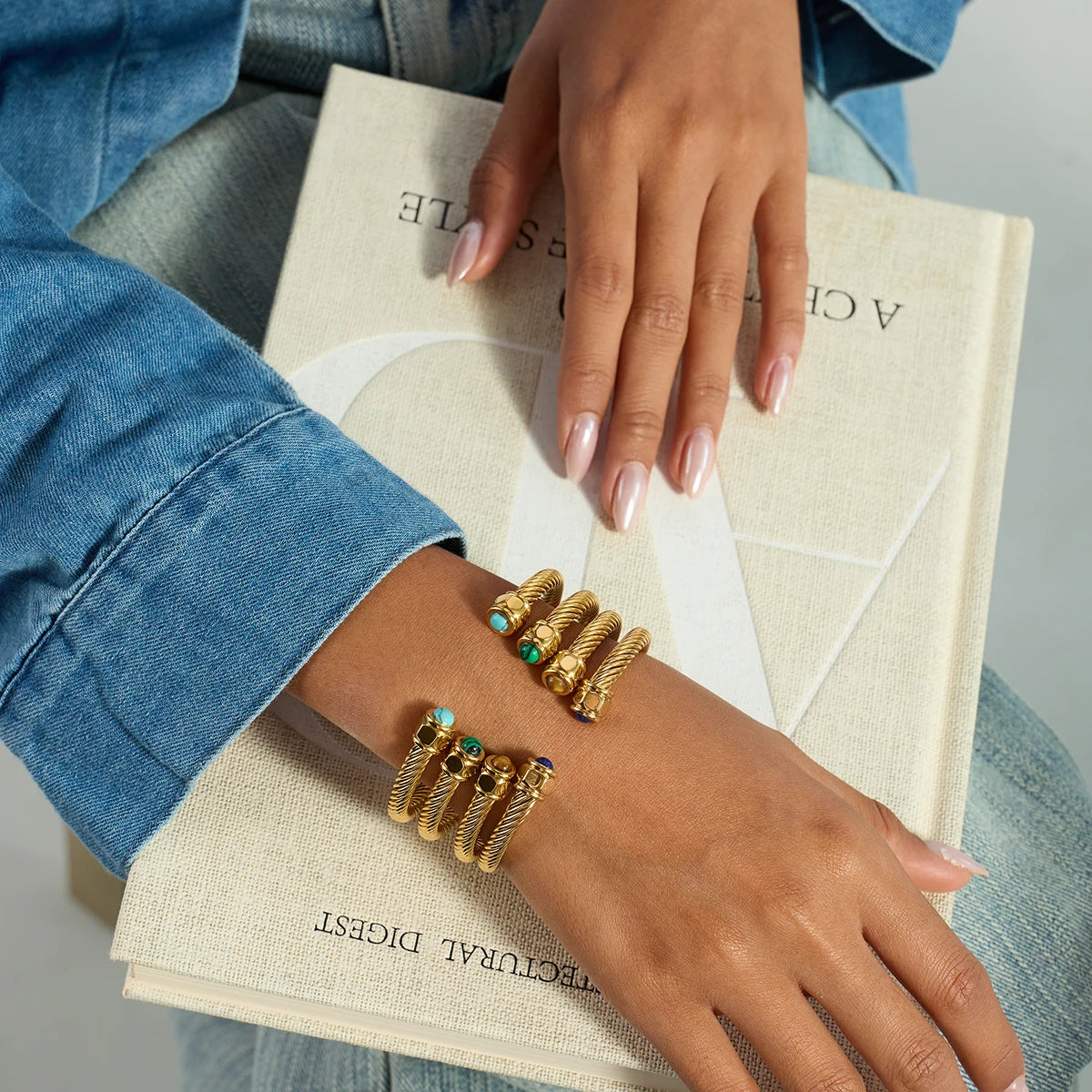 Hand wearing gold bracelets with turquoise stones on a book