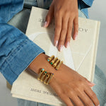 Hand wearing gold bracelets with turquoise stones on a book