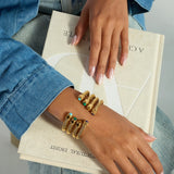 Hand wearing gold bracelets with turquoise stones on a book
