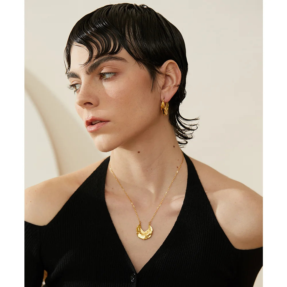 Woman wearing gold earrings and necklace against a neutral background