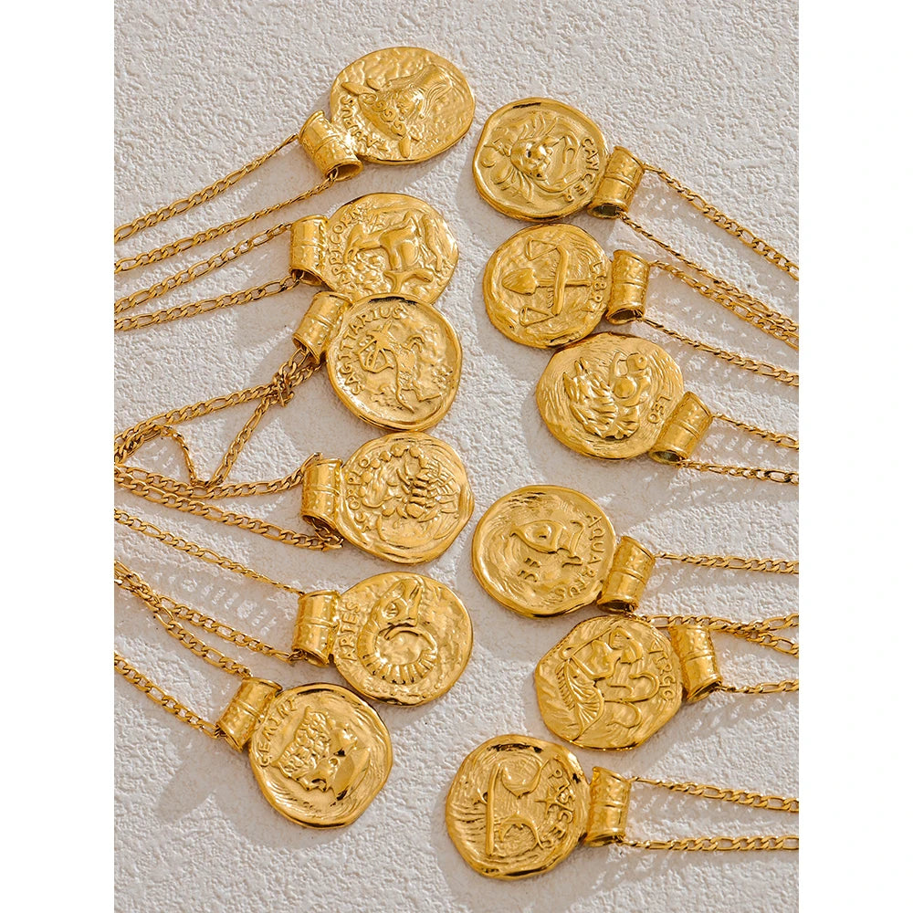 Gold zodiac necklaces with coin pendants on a textured white background