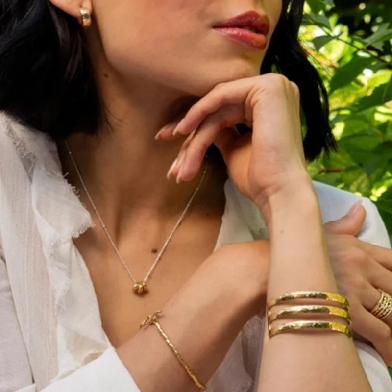 Woman wearing gold jewelry with a blurred green background