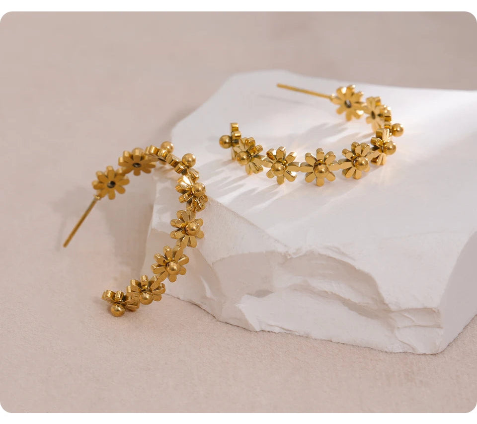 Gold floral hoop earrings on a white fabric background with 'HAPPY' branding.
