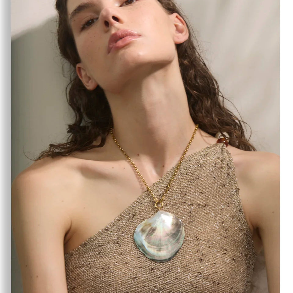 Woman wearing a gold necklace with a large pendant against a neutral background