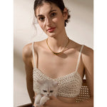 Woman wearing a decorative top holding a kitten against a neutral background