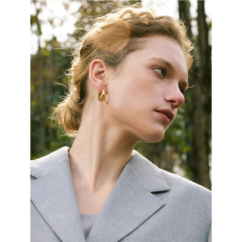 Woman wearing gold hoop earrings with a blurred natural background
