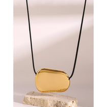 Gold pendant on a black cord against a neutral background