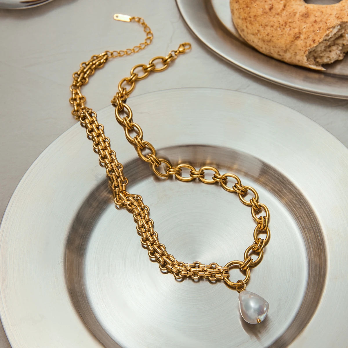 Gold chain necklace with a pearl pendant on a white plate