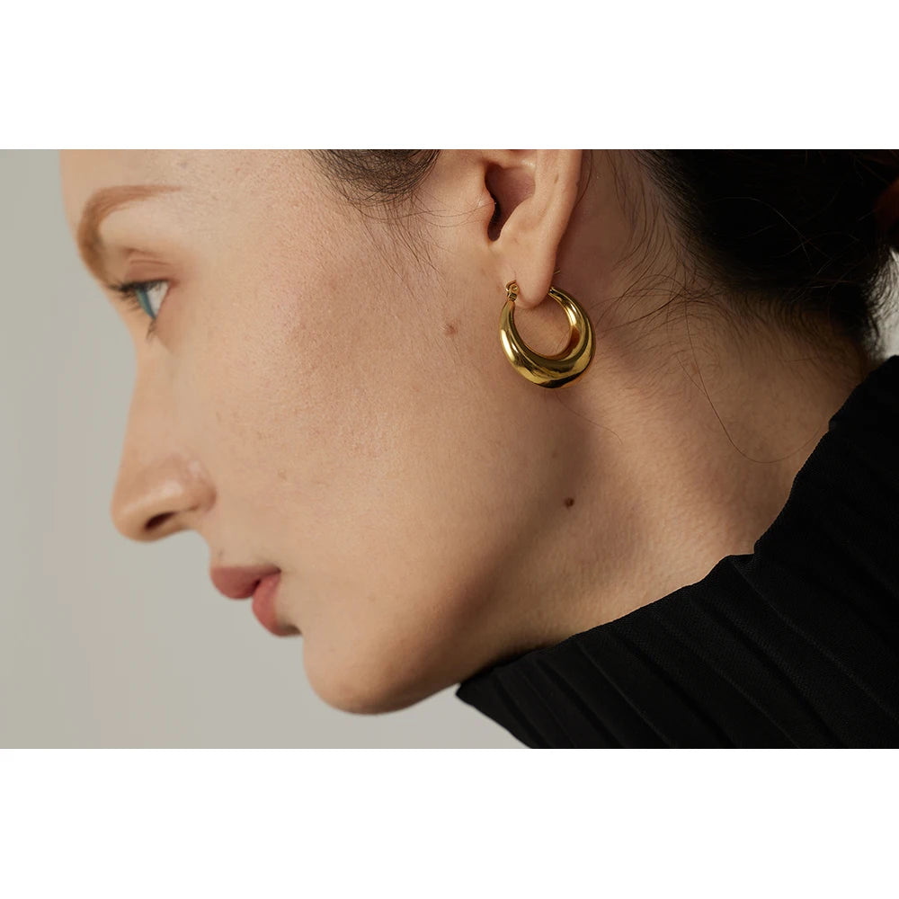 Close-up of a person wearing a gold hoop earring against a neutral background