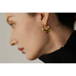 Close-up of a person wearing a gold hoop earring against a neutral background