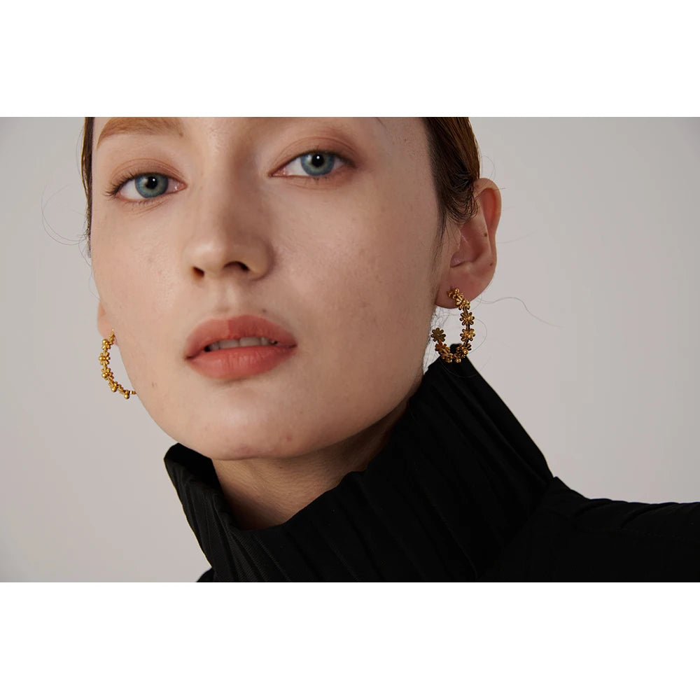 Close-up of a person wearing gold hoop earrings with a neutral background