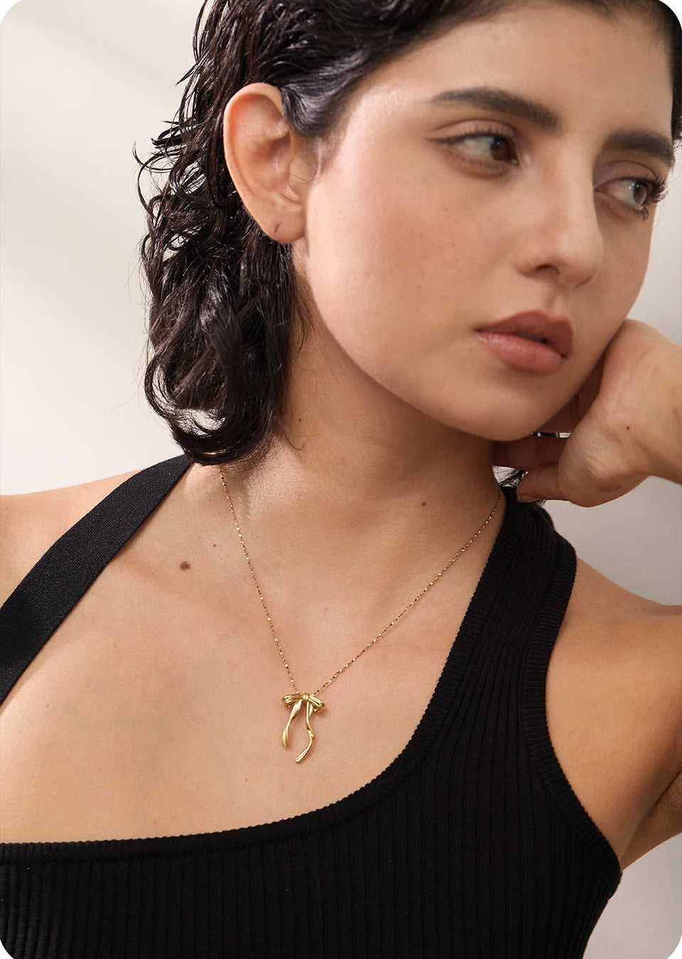 Woman wearing a gold necklace with a delicate pendant against a neutral background