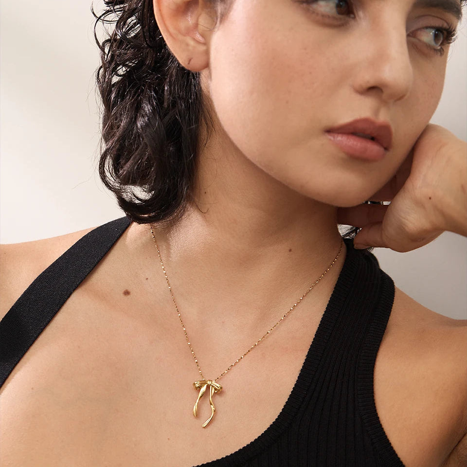 Woman wearing a gold necklace with a delicate pendant against a neutral background