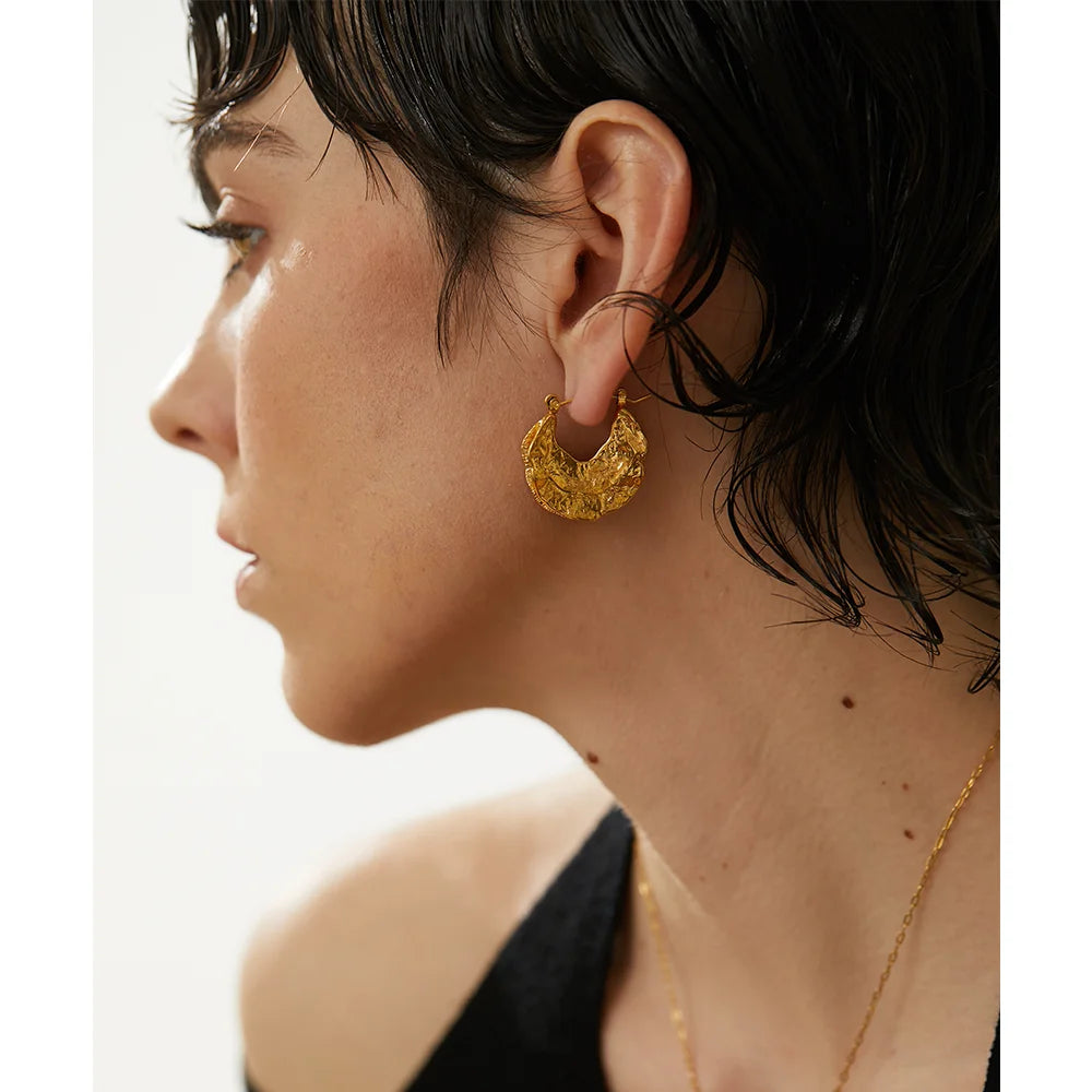 Close-up of a woman wearing gold hoop earrings with a blurred background