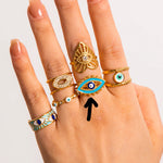 Hand wearing multiple gold and turquoise rings with eye designs on a light background