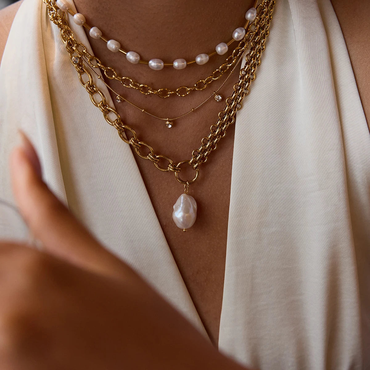Close-up of layered gold necklaces with pearl pendants on a person wearing a white top.