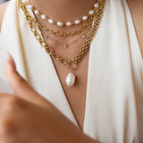 Close-up of layered gold necklaces with pearl pendants on a person wearing a white top.