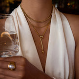 Person wearing gold necklaces and a ring, holding a glass with a blurred background