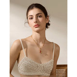 Woman wearing a beige crochet top and gold necklace with a red pendant.
