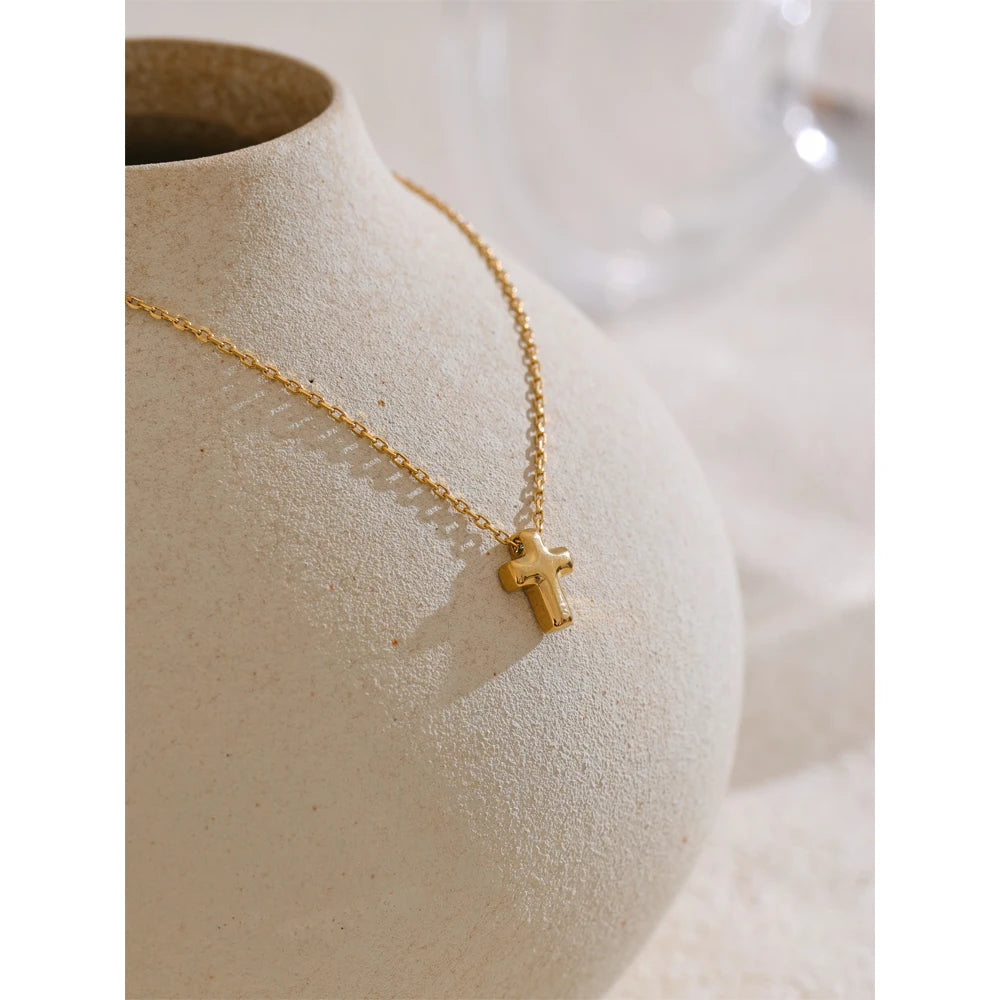 Gold necklace with a cross pendant on a textured beige surface