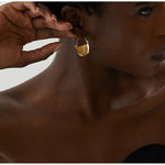 Gold earring being worn by a person with a neutral background