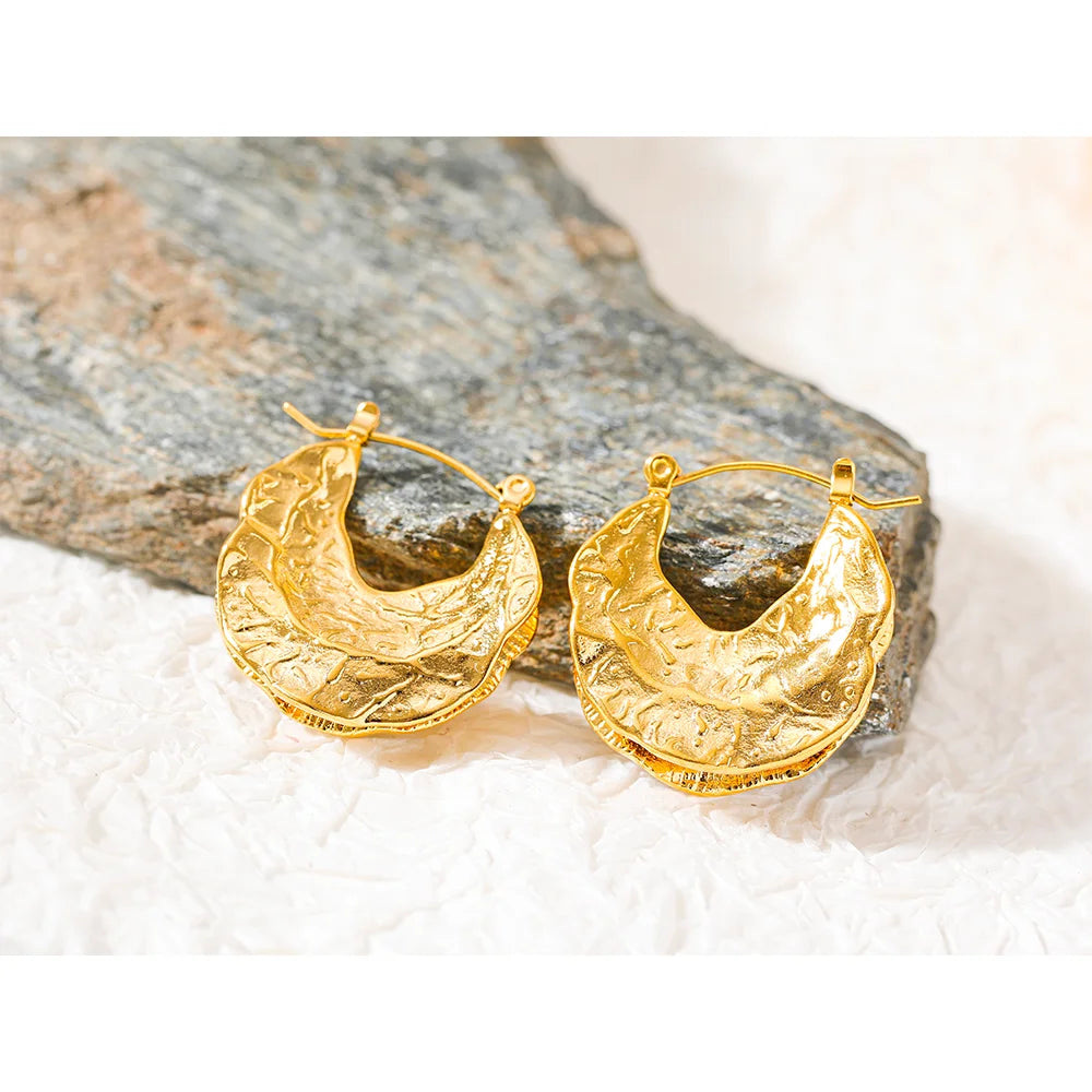 Gold hoop earrings on a stone surface