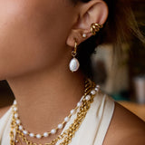 Close-up of an ear with gold and pearl earrings and necklaces.