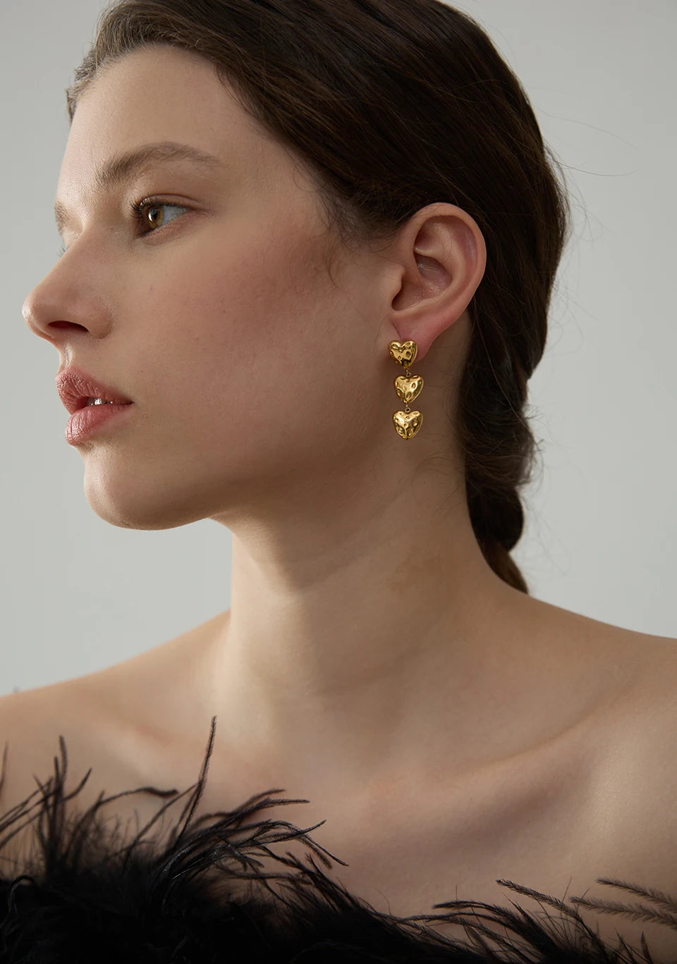 Woman wearing gold heart-shaped earrings with a neutral background