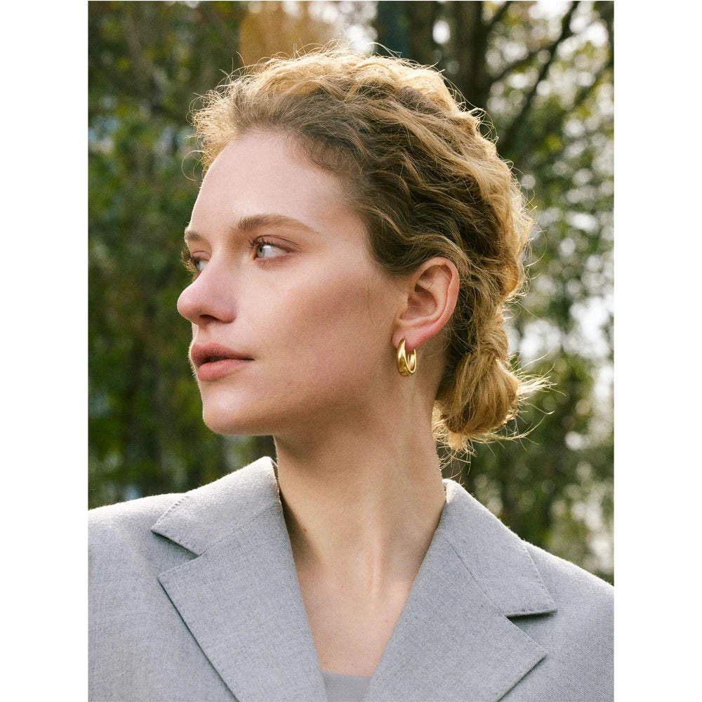 Woman wearing a gold hoop earring from Ezra Gems in a gray blazer with a blurred natural background