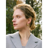 Woman wearing a gold hoop earring from Ezra Gems in a gray blazer with a blurred natural background