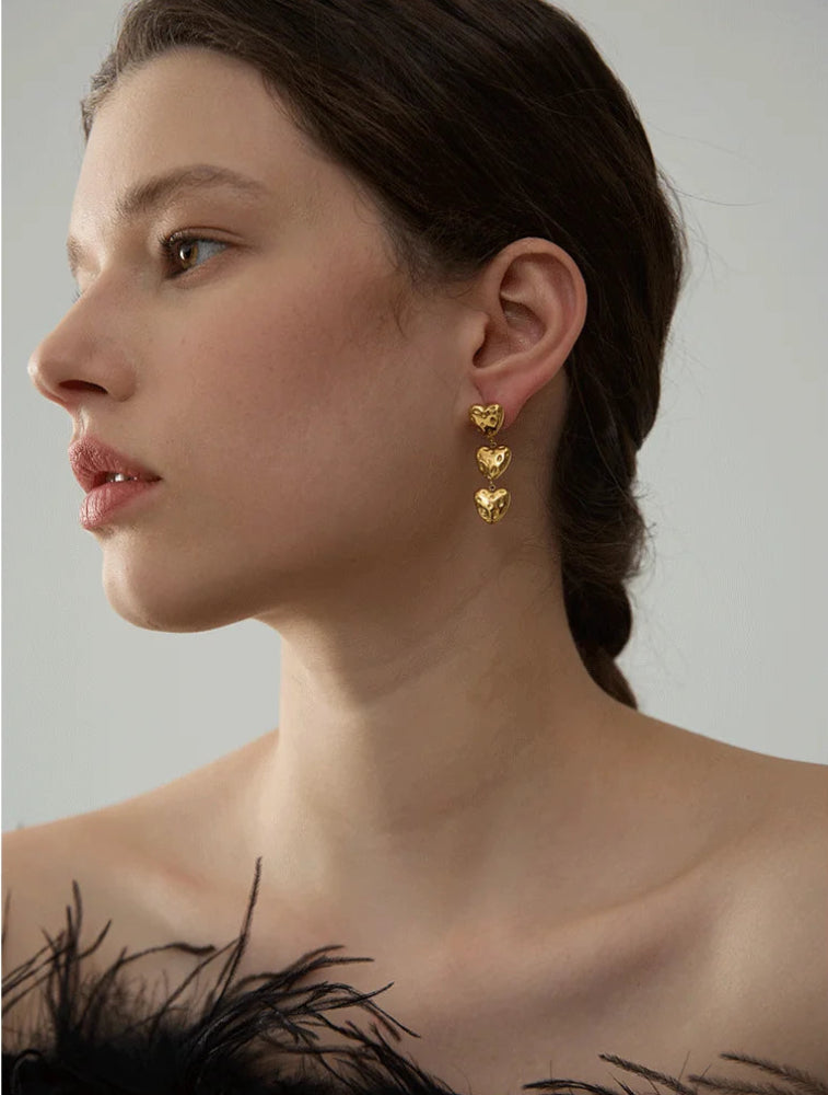 Woman wearing gold heart-shaped earrings against a neutral background